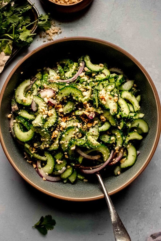 Overhead shot of Thai Cucumber Salad in green bowl with spoon next to bunch of cilantro.