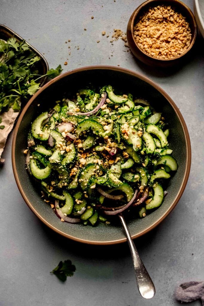 Overhead shot of Thai Cucumber Salad in green bowl with spoon next to bunch of cilantro.