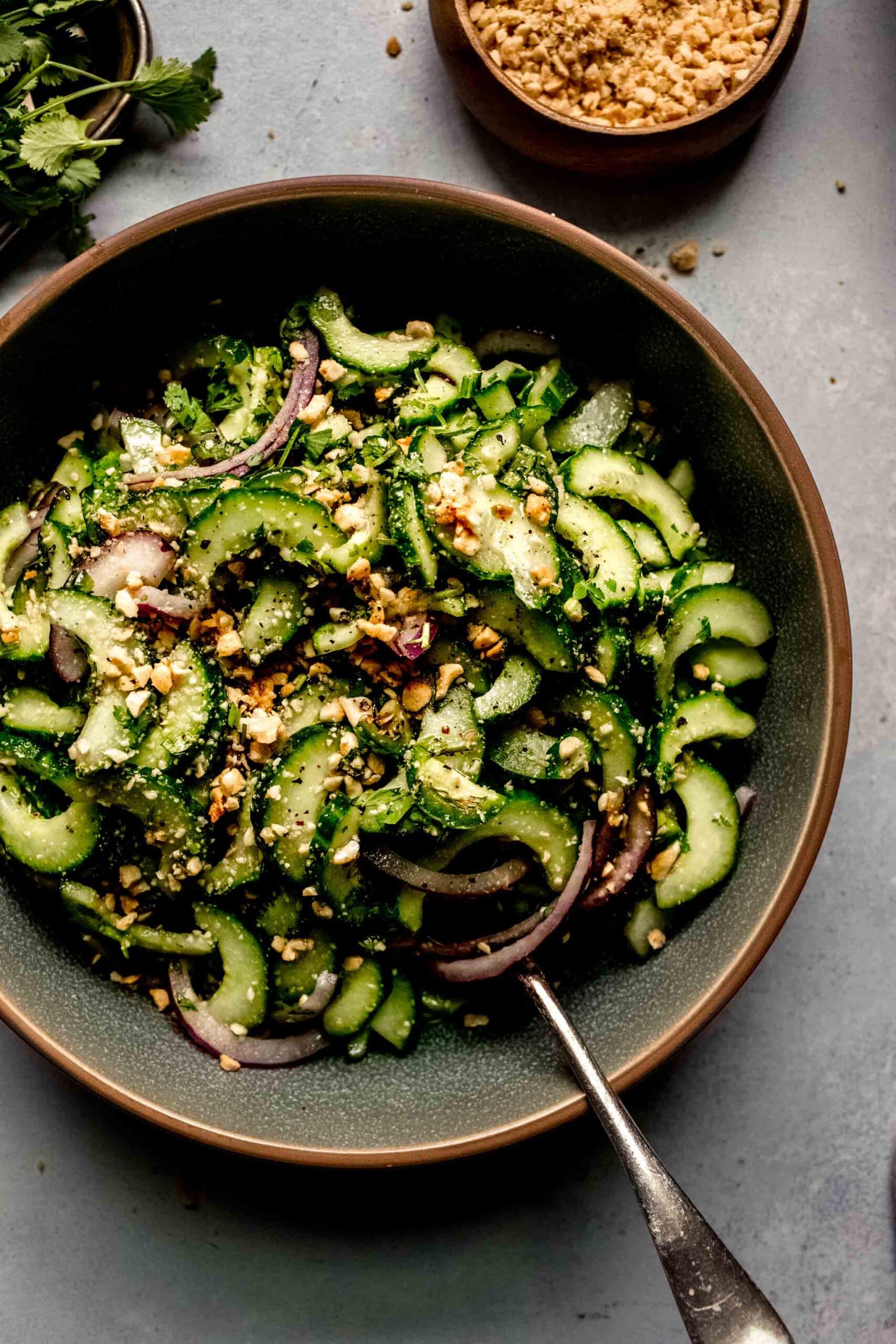 Thai cucumber salad in green bowl next to small bowl of chopped peanuts.