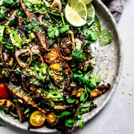 Overhead shot of thai mushroom salad on speckled grey plate with lime wedges.