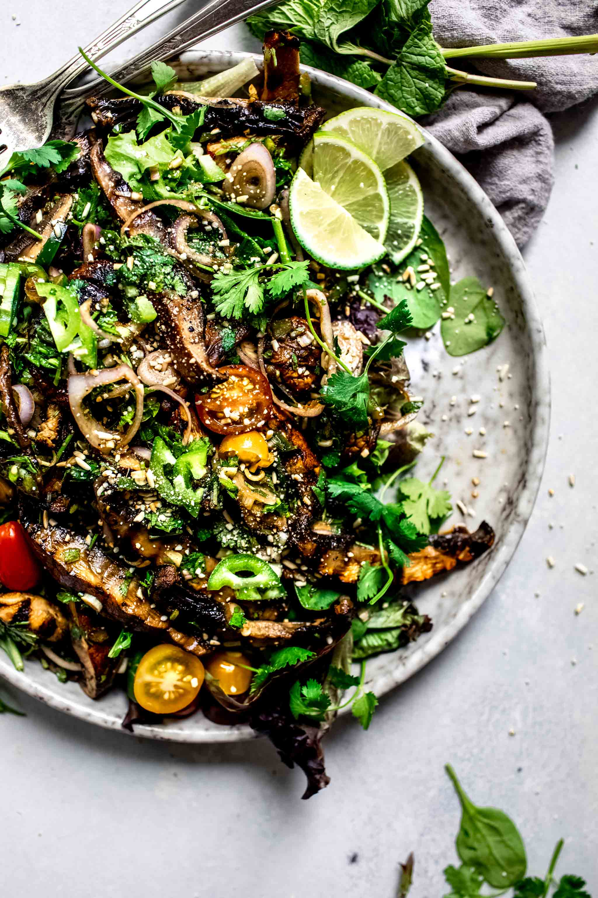 Overhead shot of thai mushroom salad on speckled grey plate with lime wedges.