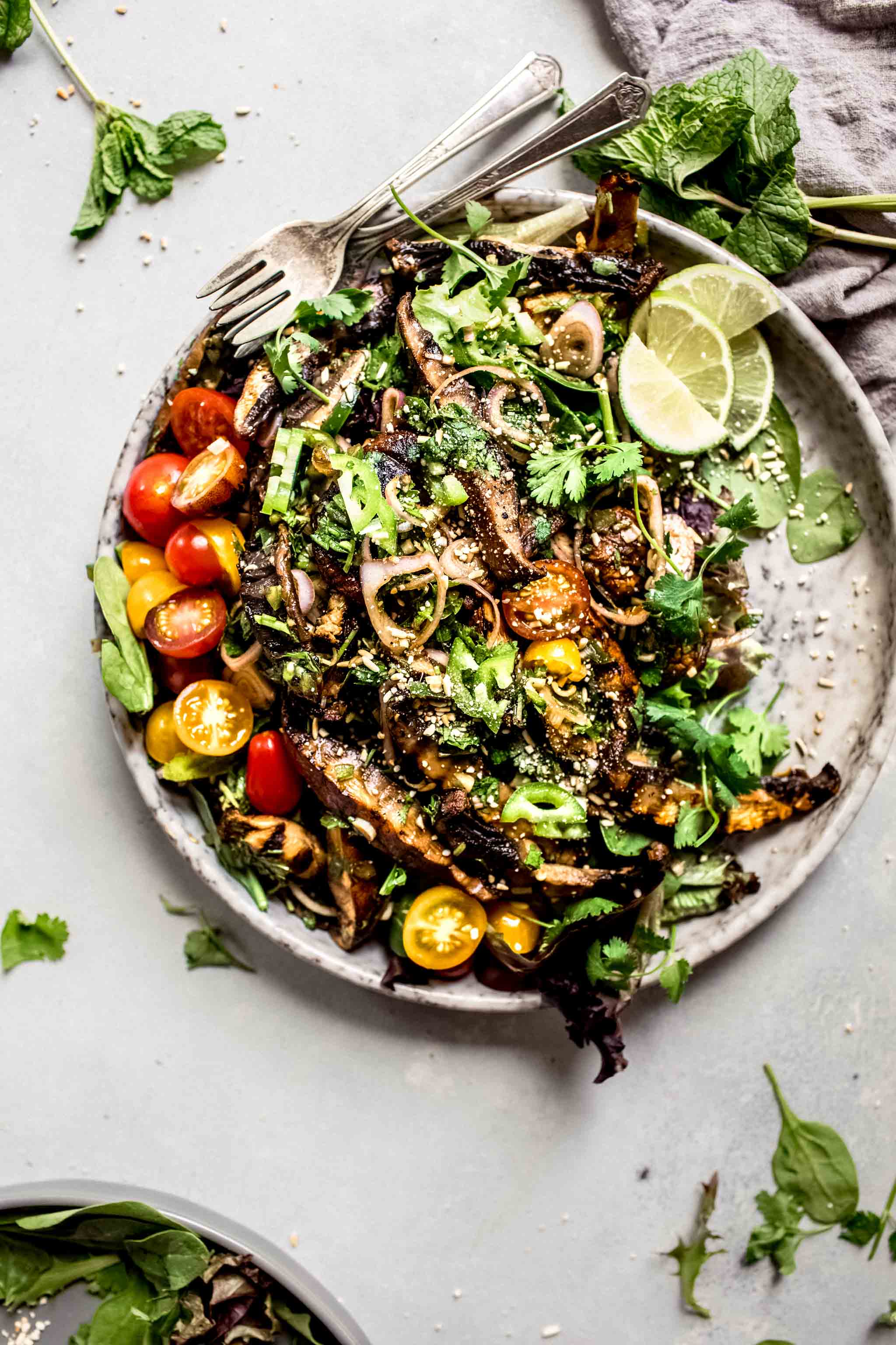 Overhead shot of thai mushroom salad on speckled grey plate with lime wedges.