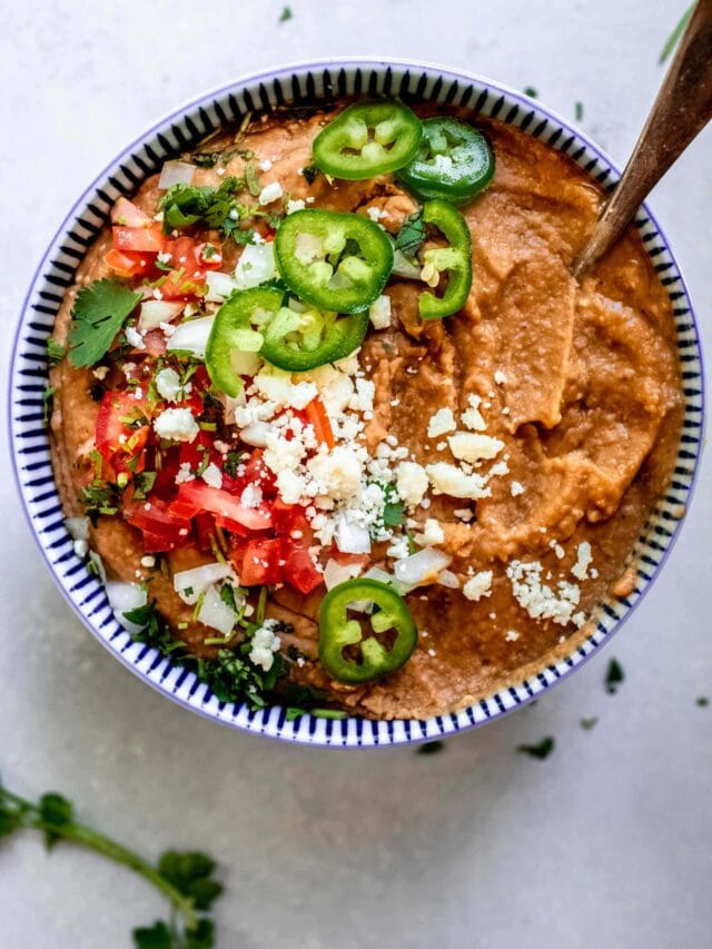 Overhead shot of refried beans in blue bowl topped with crumbled cotija, tomatoes and jalapenos.
