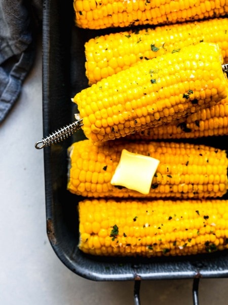 Ears of corn on the cob in a grey serving dish with a pat of butter and sprinkling of parsley.