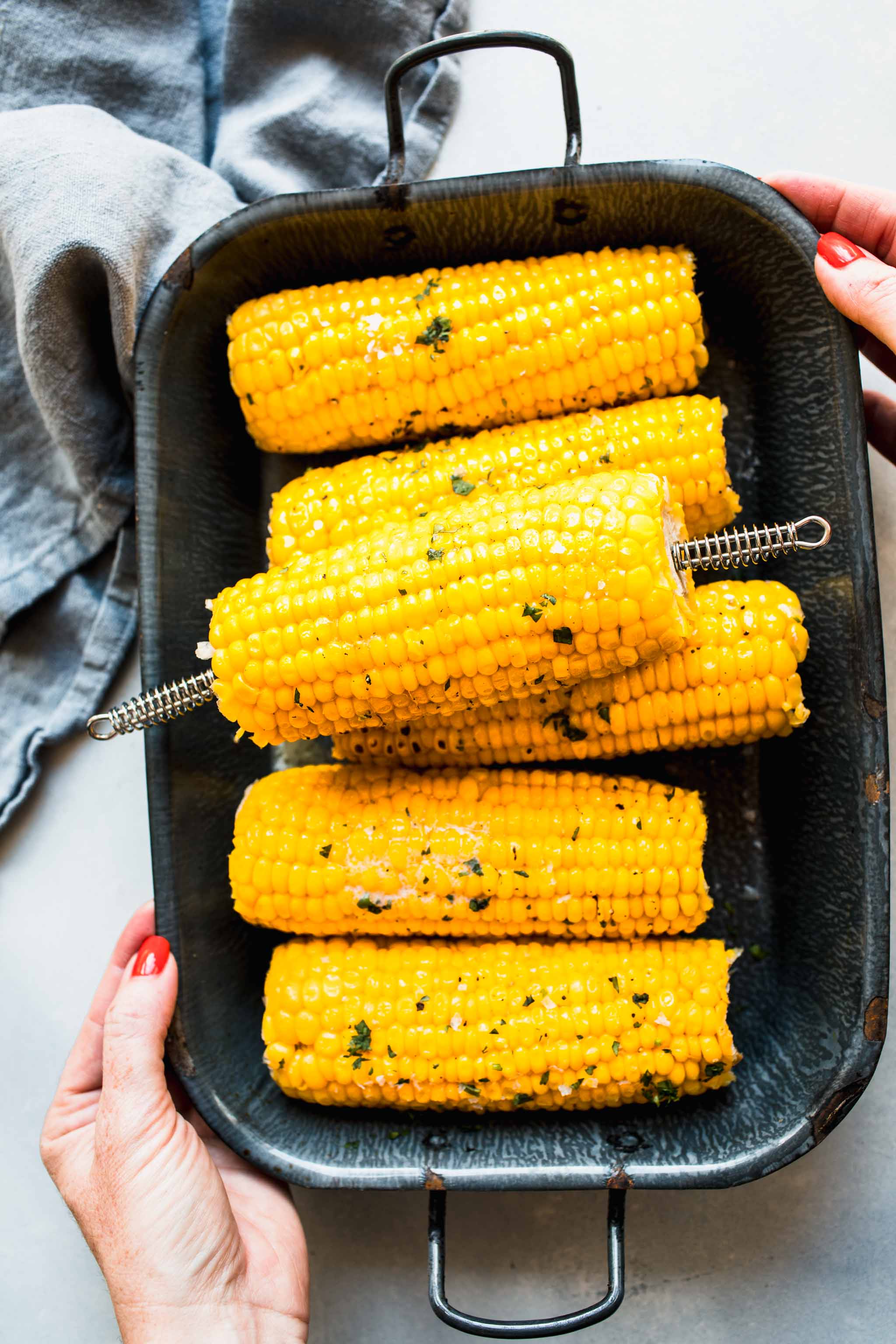 Hand holding platter of cooked corn on the cob. 