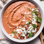 Overhead shot of refried beans in white bowl topped with cilantro and cotija cheese.