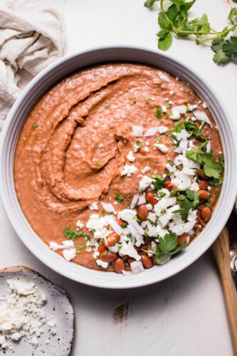 Overhead shot of refried beans in white bowl topped with cilantro and cotija cheese.