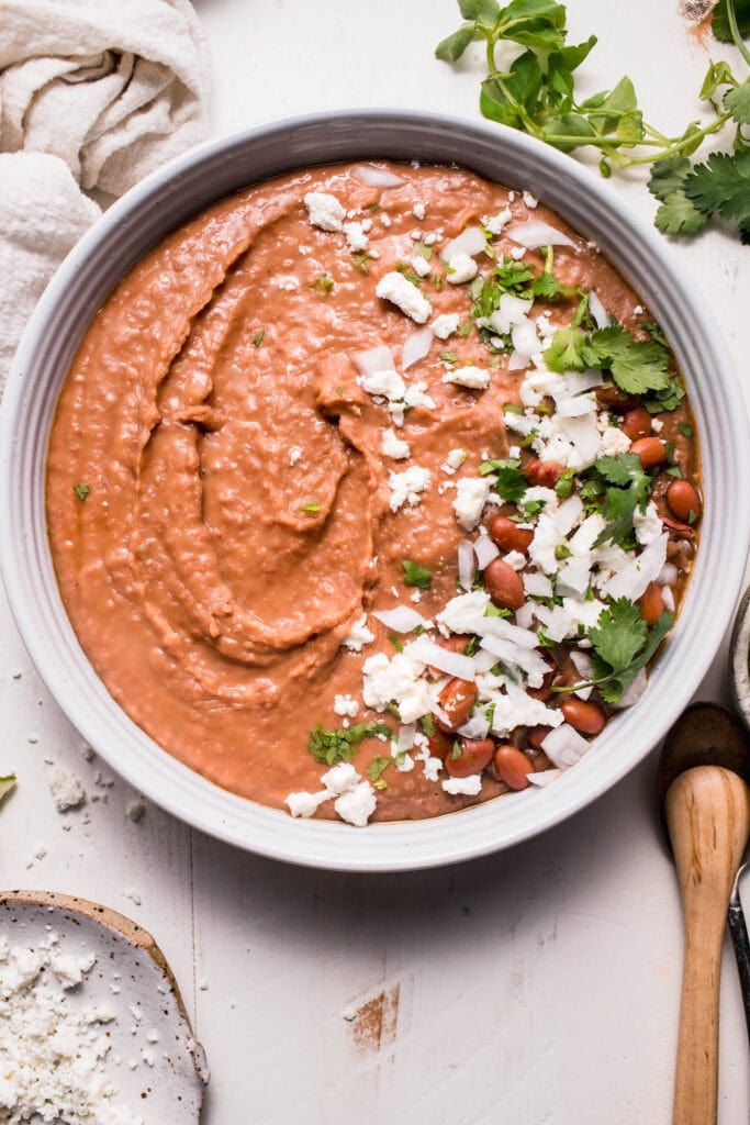 Overhead shot of refried beans in white bowl topped with cilantro and cotija cheese.
