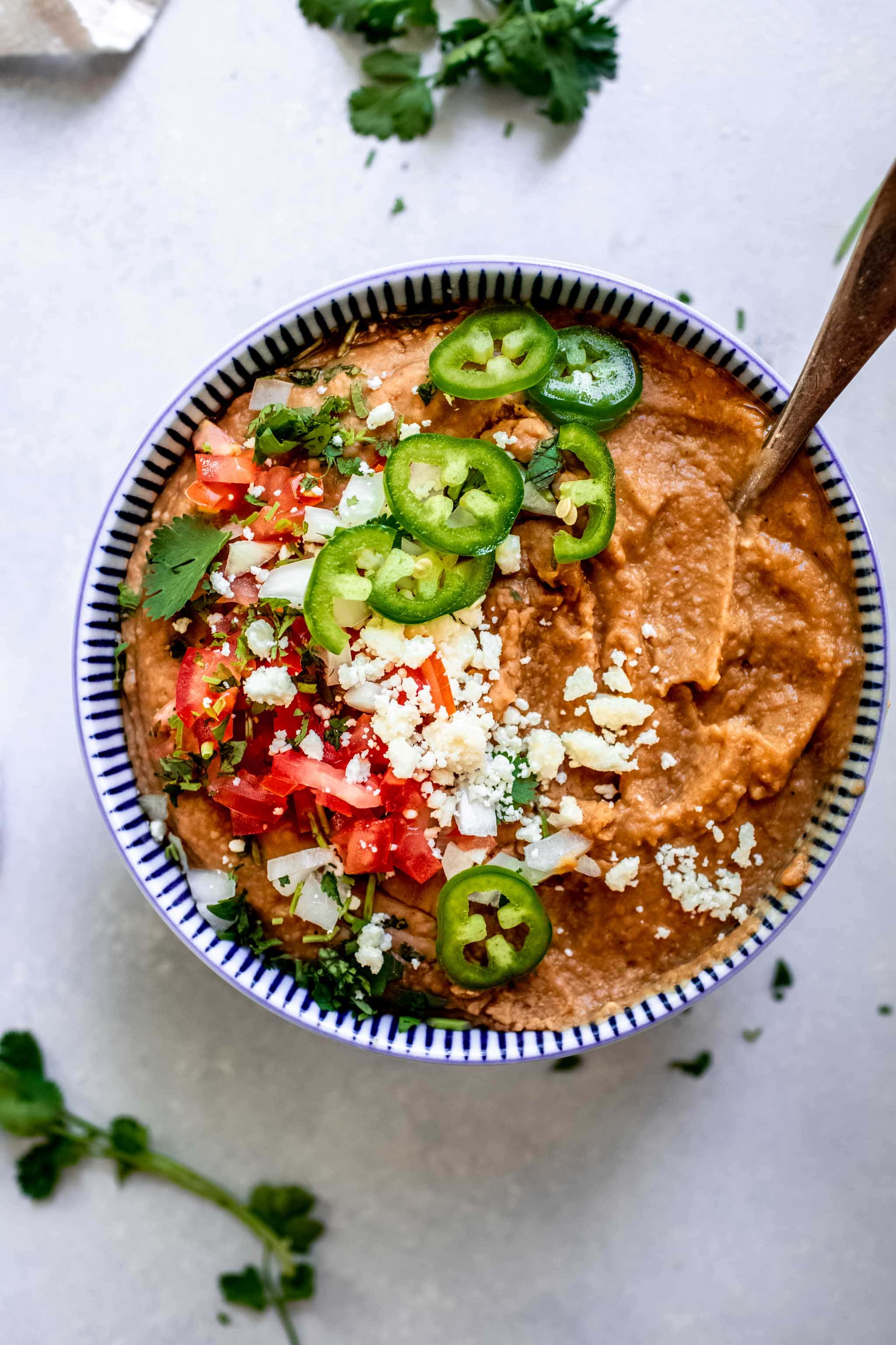 Overhead shot of refried beans in blue bowl topped with crumbled cotija, tomatoes and jalapenos.