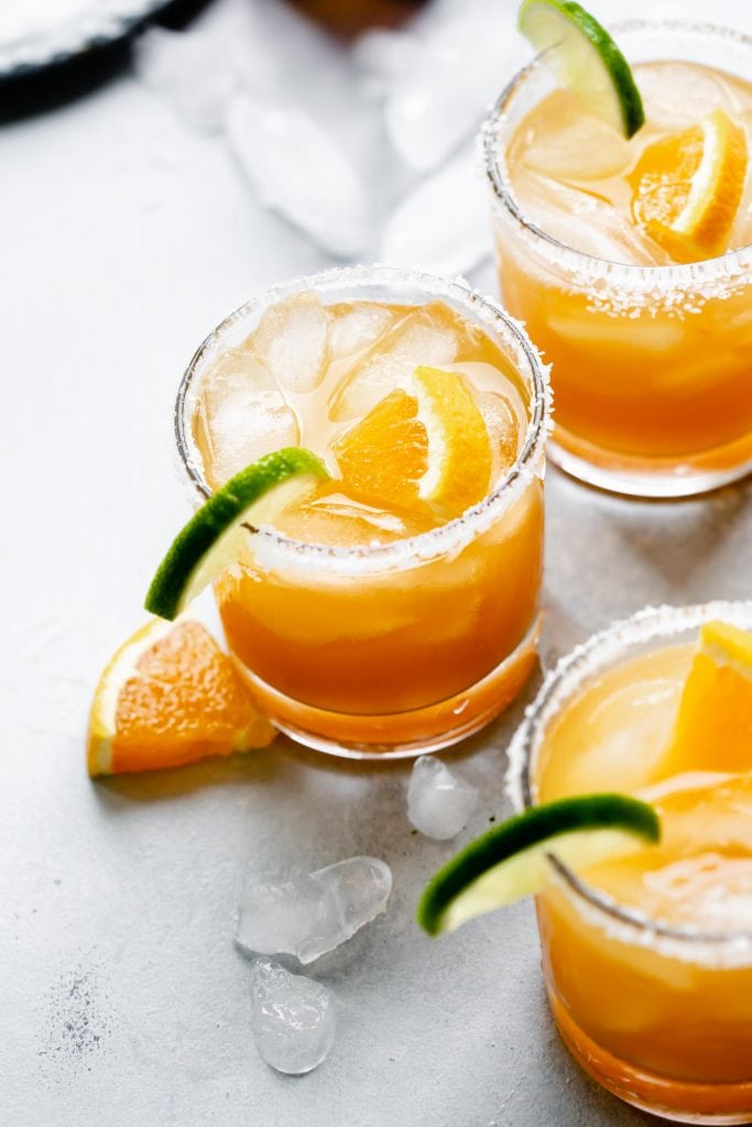 Three glasses of Italian Margarita rimmed with salt and garnished with orange and lime slices.