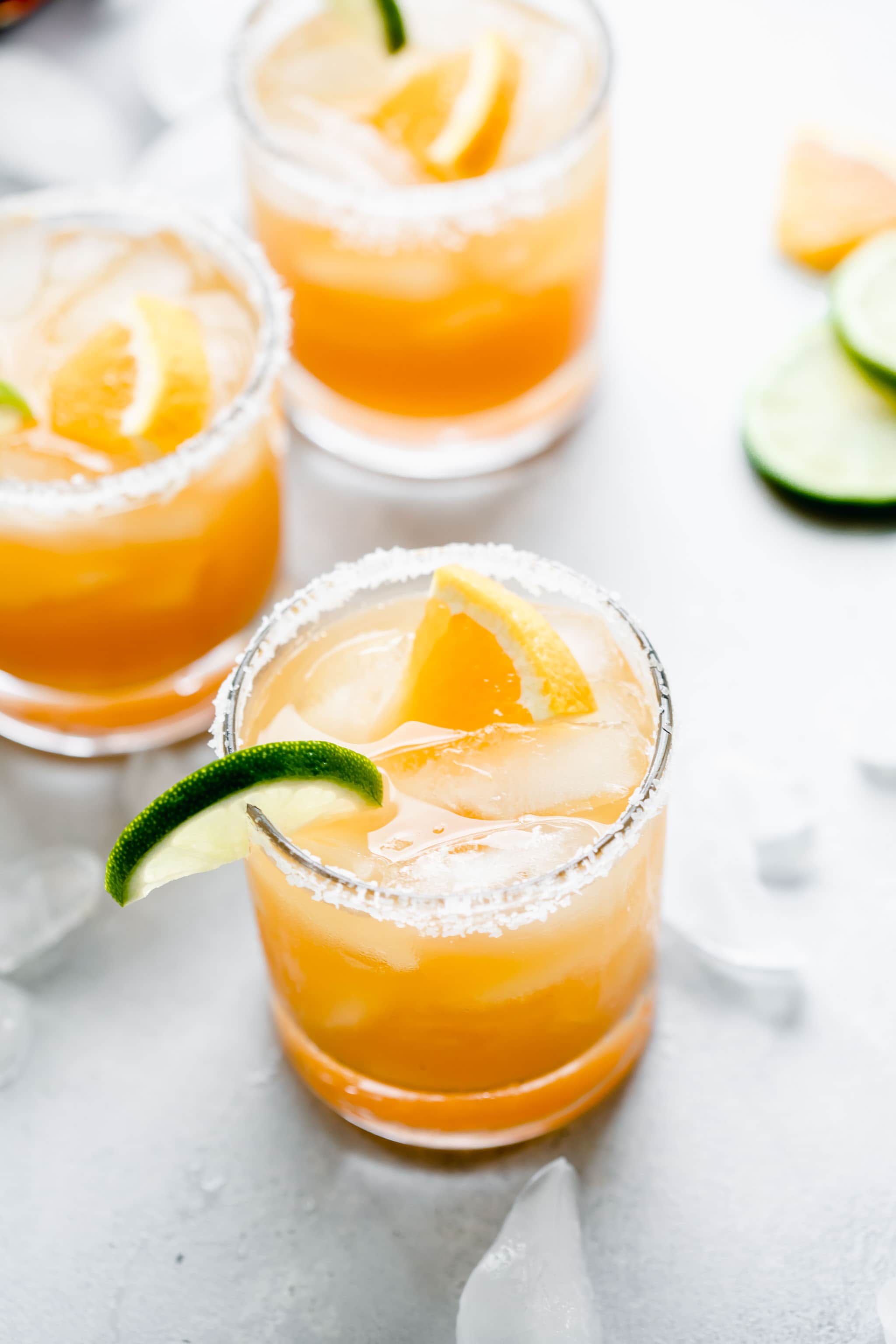 Three glasses of Italian Margarita rimmed with salt and garnished with orange and lime slices.