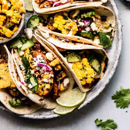 Mexican Street Corn Tacos arranged on grey plate next to bowl of corn.
