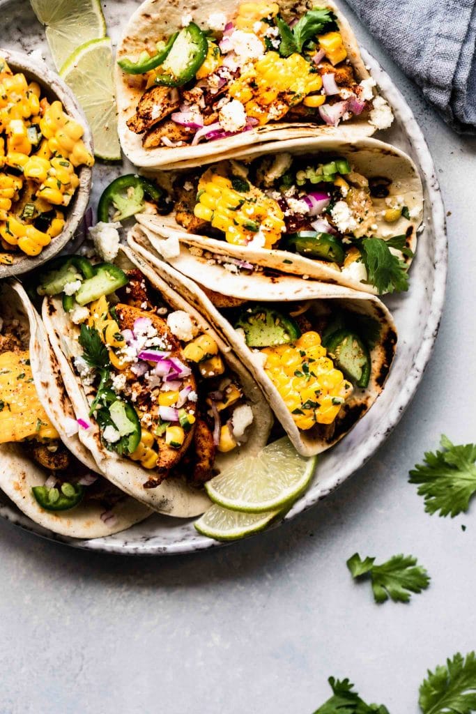 Mexican Street Corn Tacos arranged on grey plate next to bowl of corn.