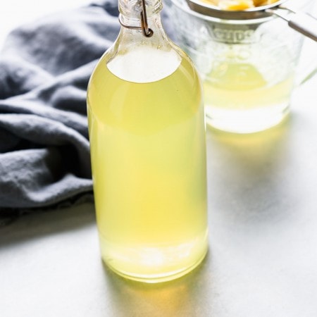 Bottle of homemade sous vide limoncello next to strainer with lemon peels.