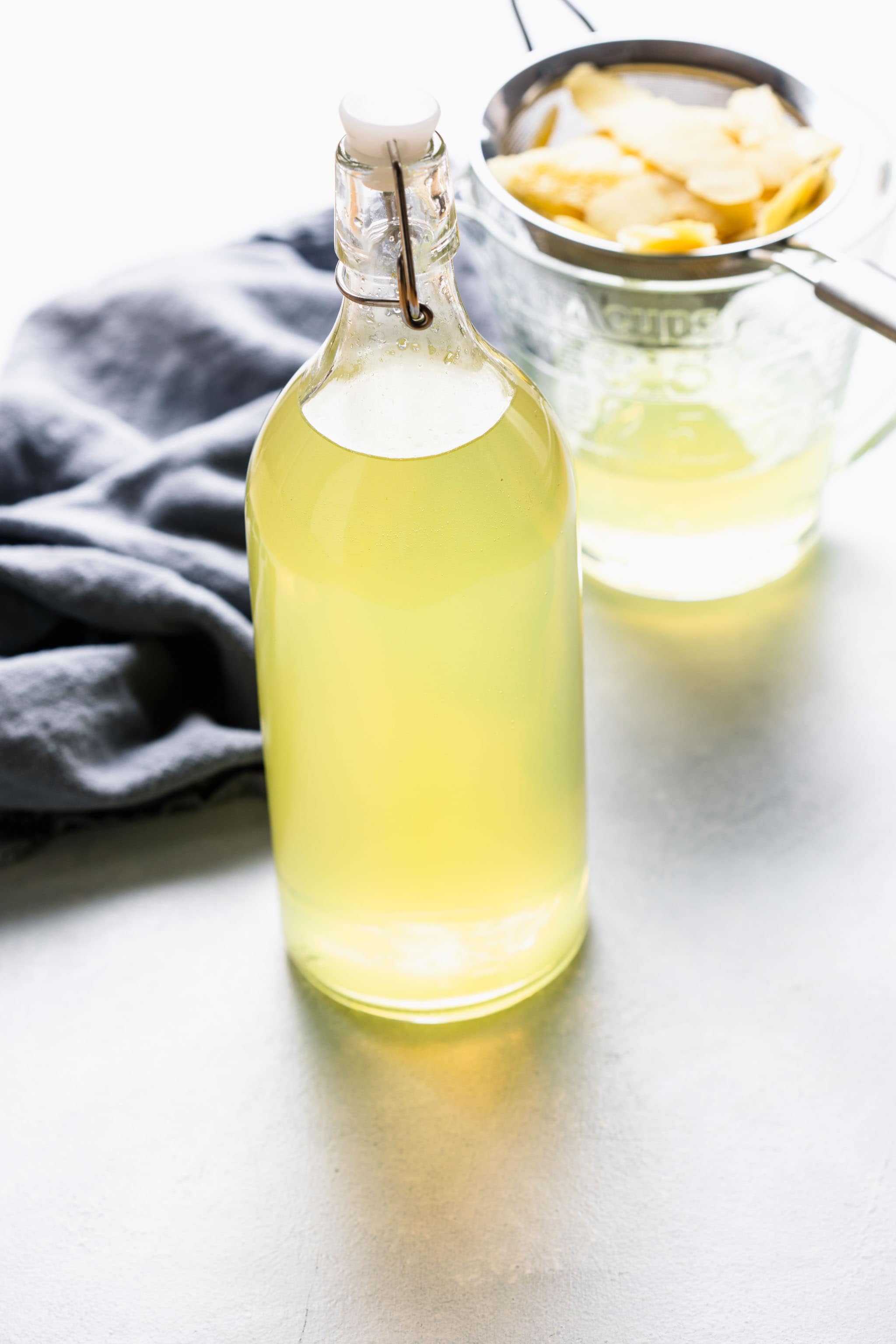 Bottle of homemade sous vide limoncello next to strainer with lemon peels.