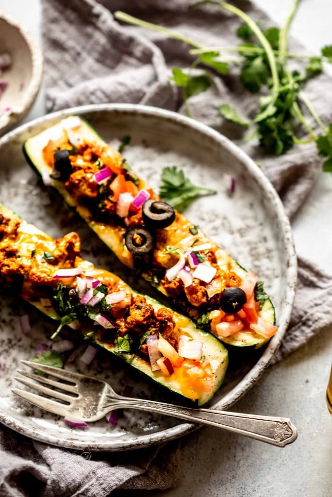 Two taco zucchini boats arranged on plate with fork. 