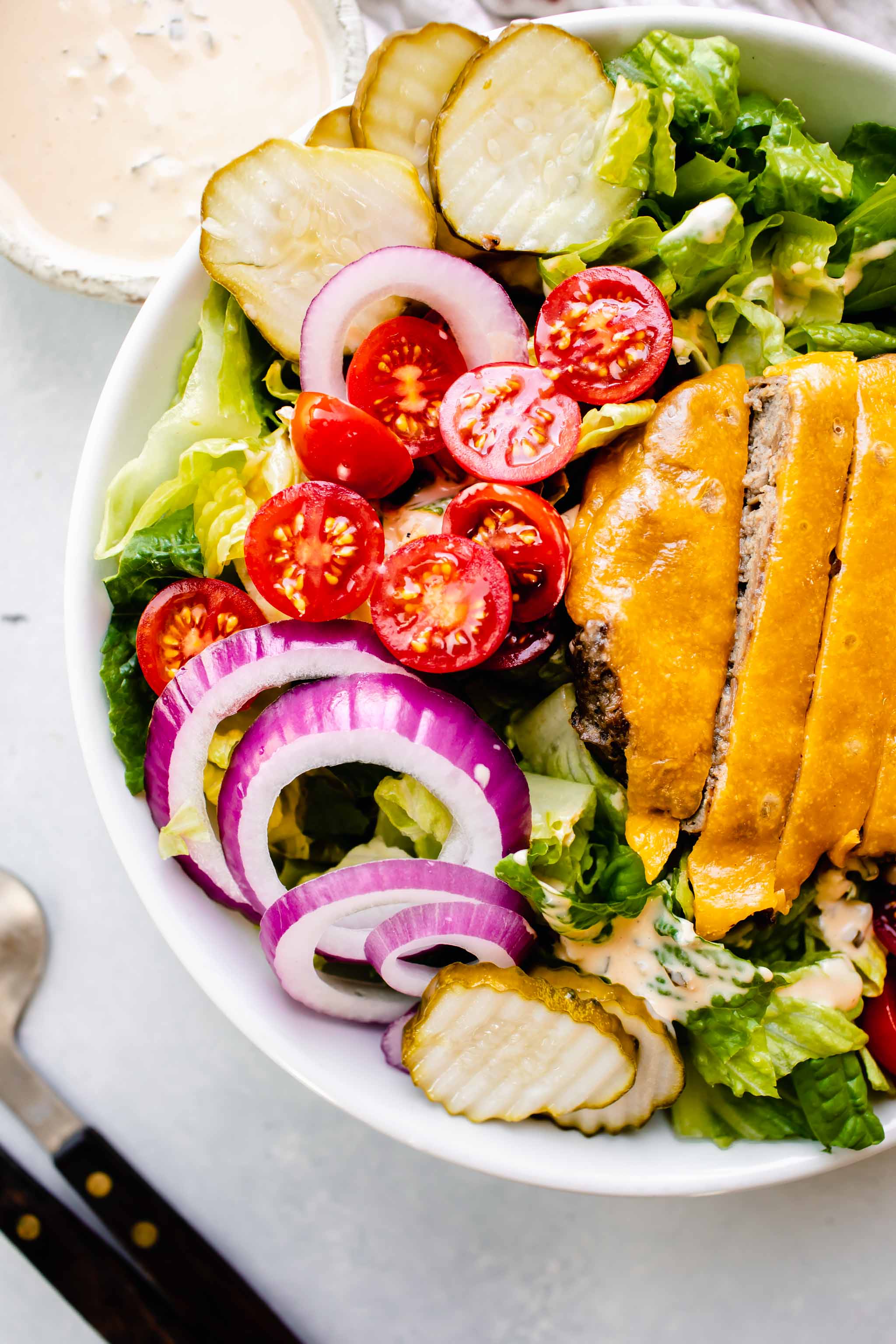 Overhead shot of cheeseburger salad in white bowl next to bowl of special sauce dressing.