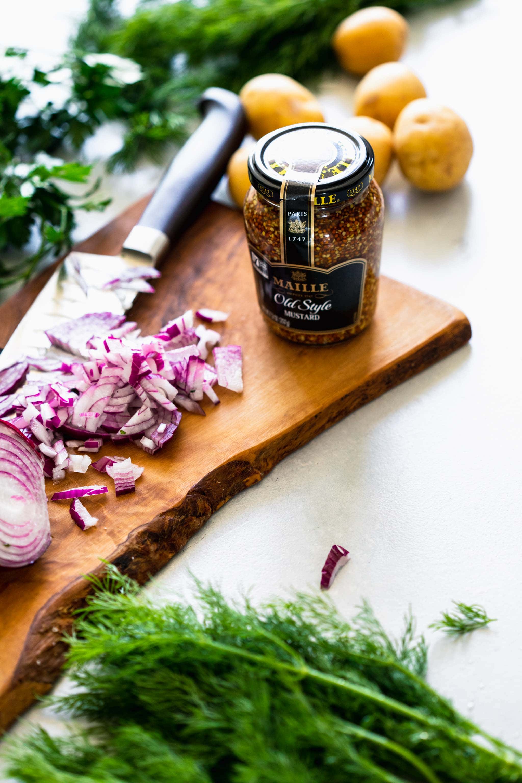 Jar of mustard next to chopped red onions on cutting board.