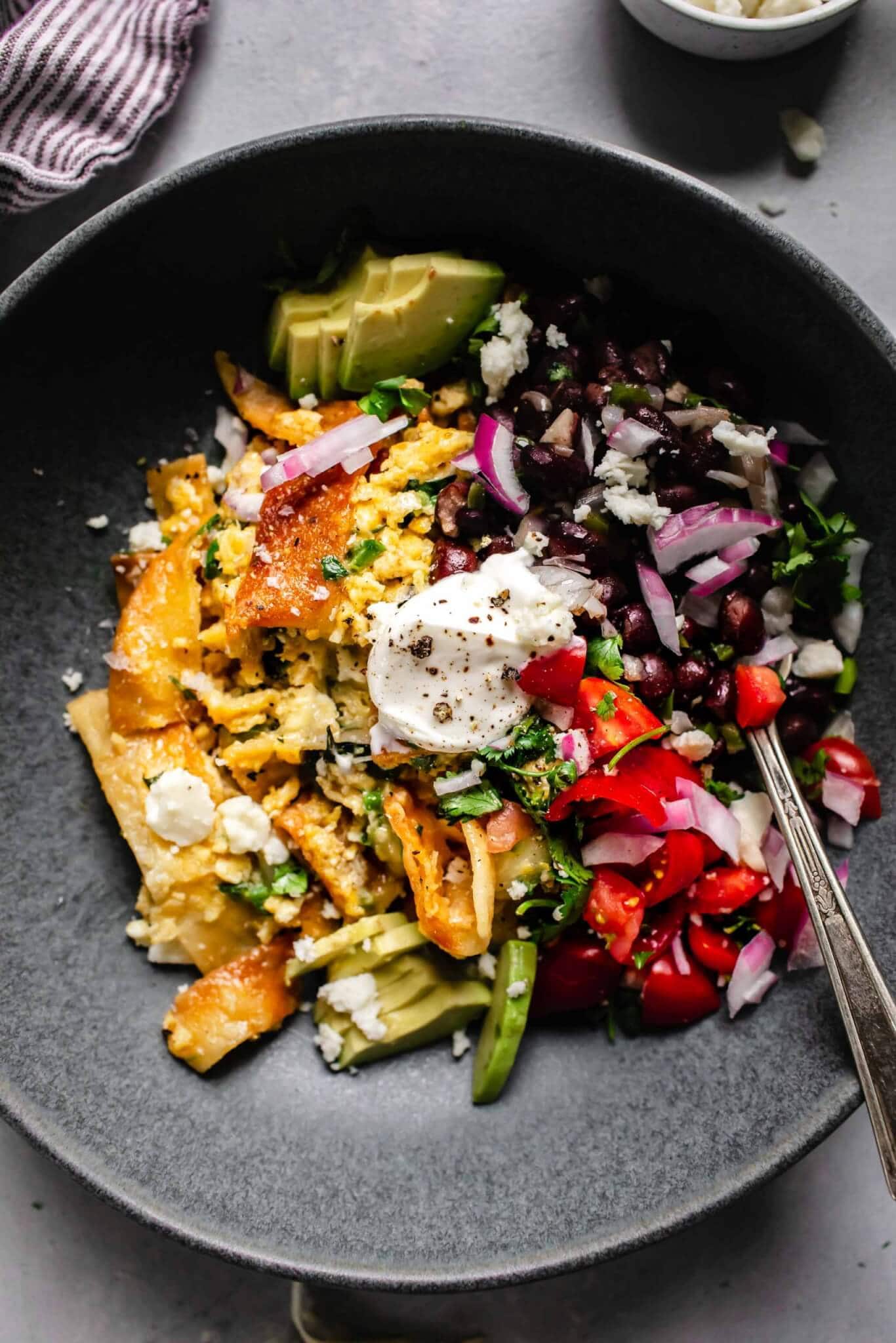 Migas in grey bowl topped with sour cream, pico and black beans.