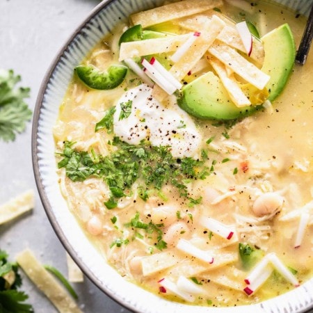 Overhead close up of bowl of instant pot white chicken chili topped with avocado, sour cream and tortilla strips.