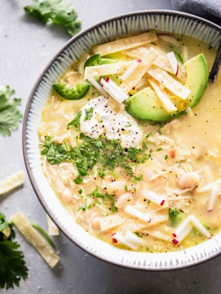 Overhead close up of bowl of instant pot white chicken chili topped with avocado, sour cream and tortilla strips.