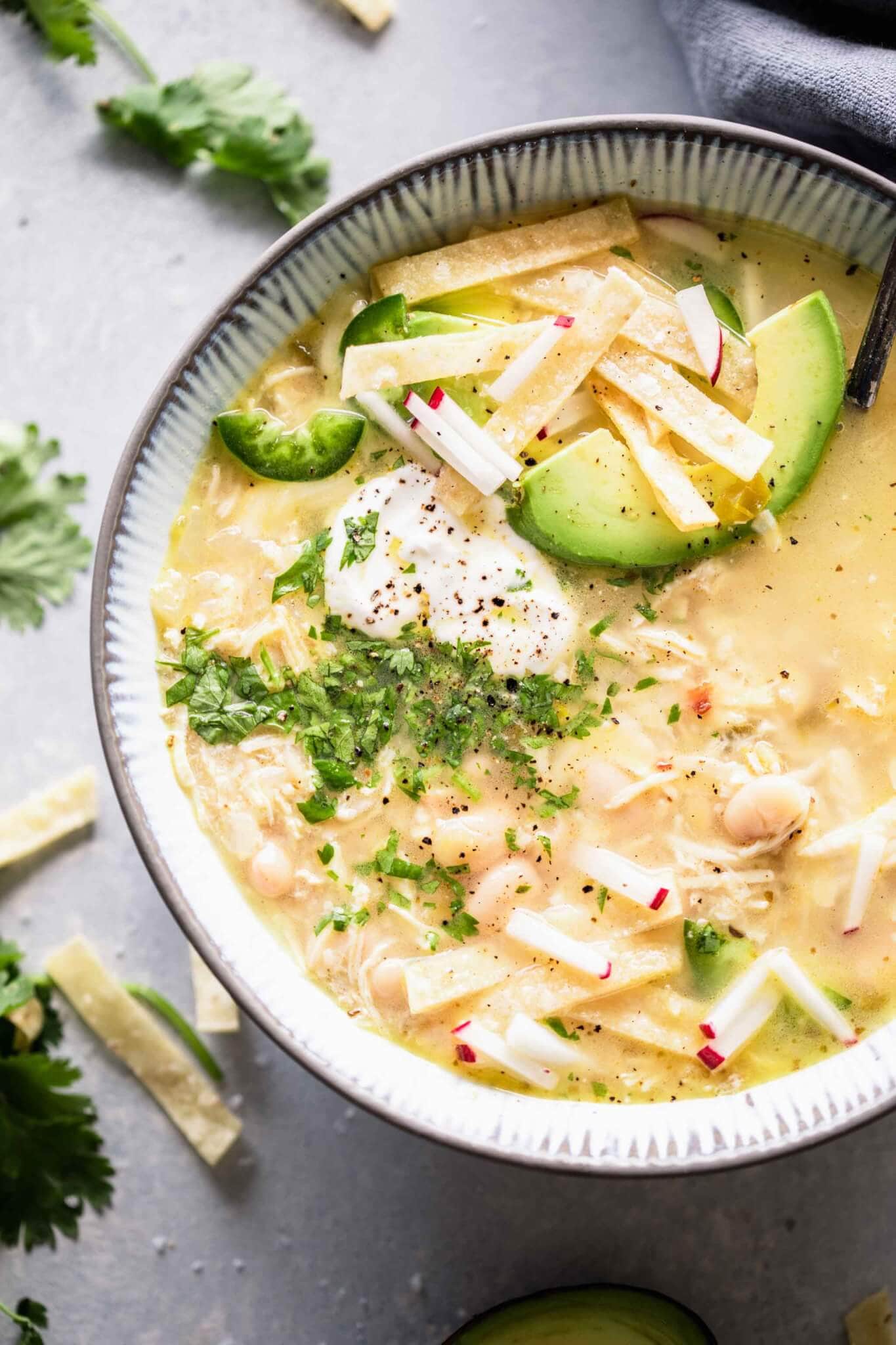 Overhead close up of bowl of instant pot white chicken chili topped with avocado, sour cream and tortilla strips.