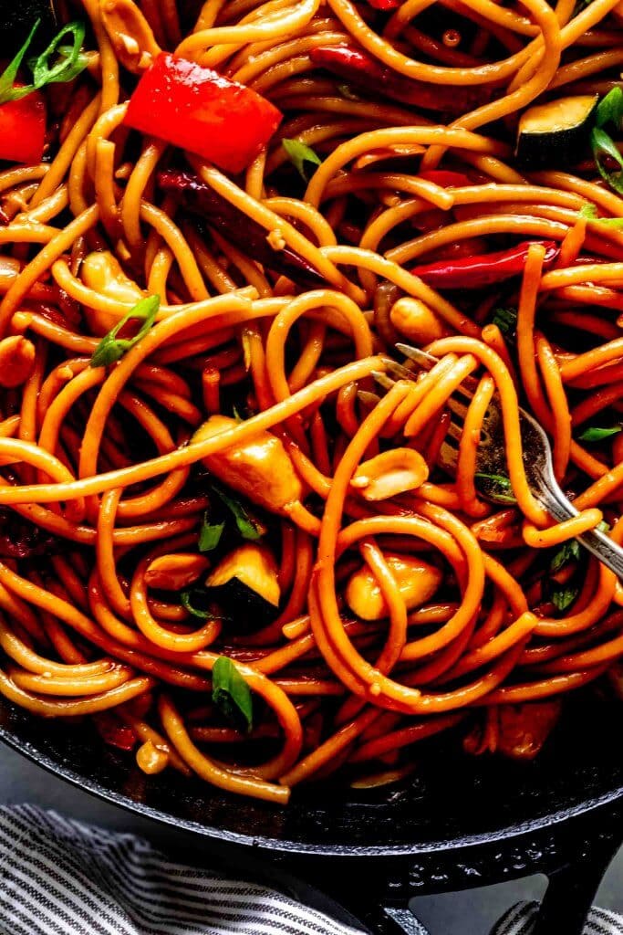 Extreme closeup of kung pao noodles with fork in skillet and pasta twirled around.