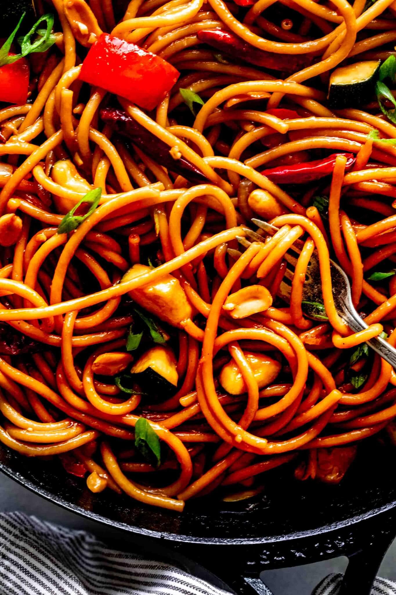 Extreme closeup of kung pao noodles with fork in skillet and pasta twirled around. 