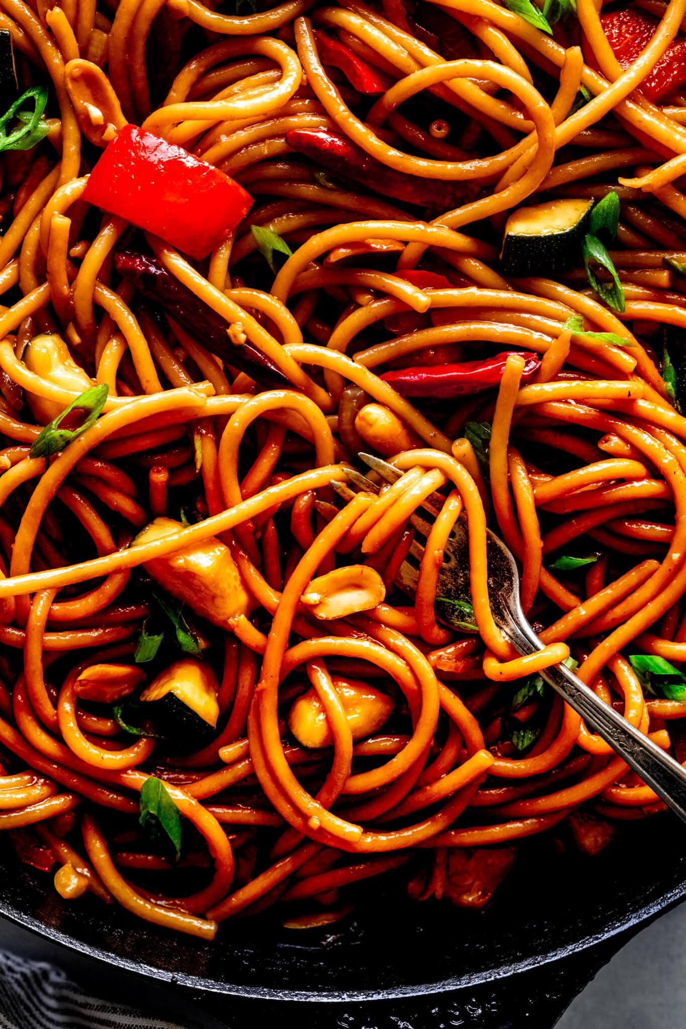 Extreme closeup of kung pao noodles with fork in skillet and pasta twirled around.