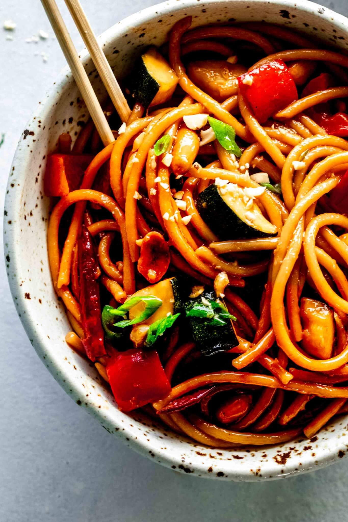 Kung pao noodles served in speckled bowl with chopsticks. 