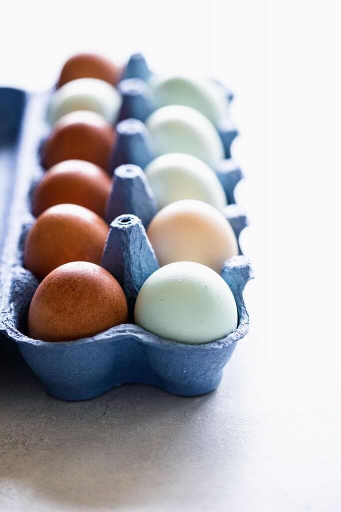 Side view of carton of eggs in blue packaging with mixture of blue, brown and peach eggs.