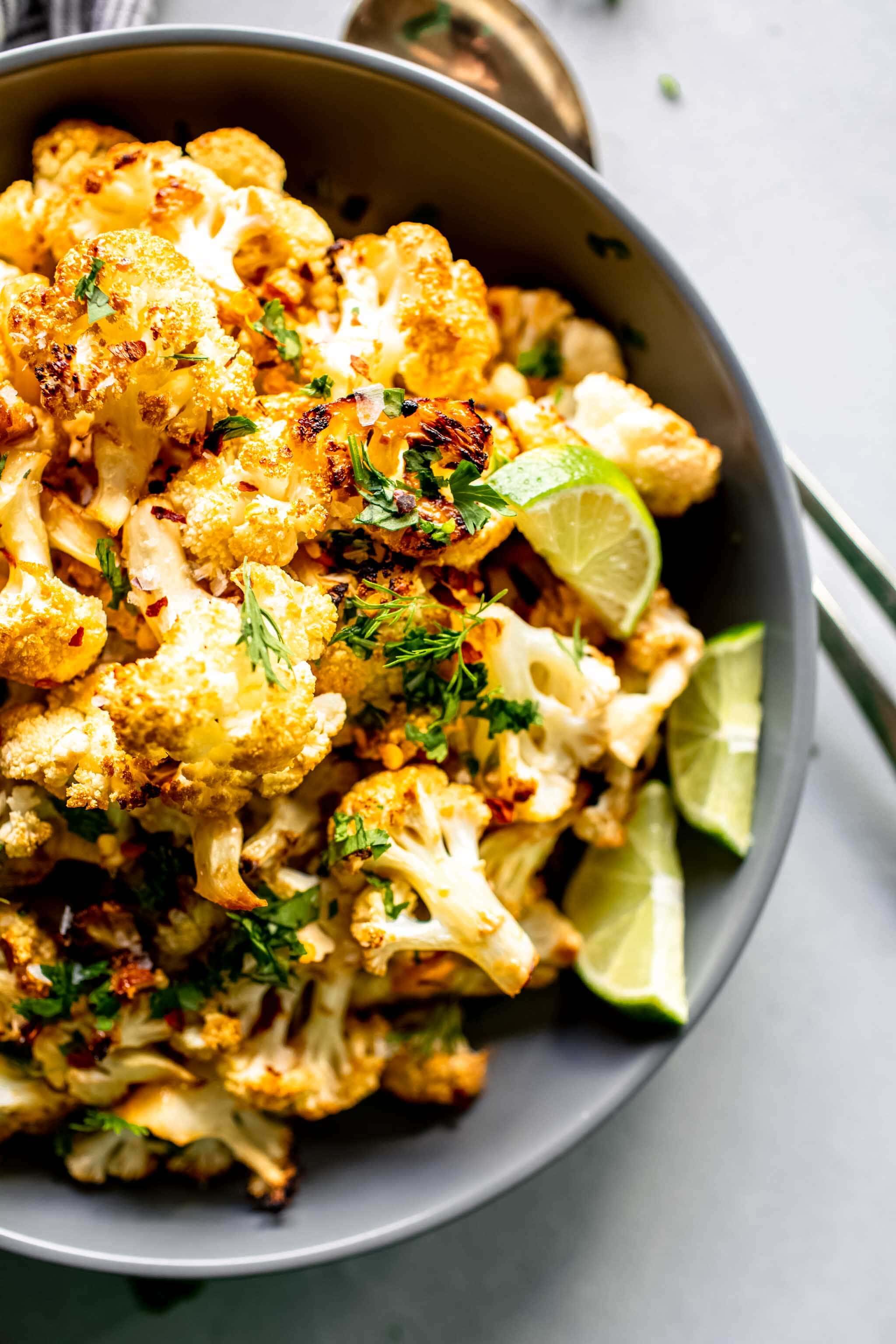 Miso roasted cauliflower in grey bowl shot from overhead and garnished with lime wedges.