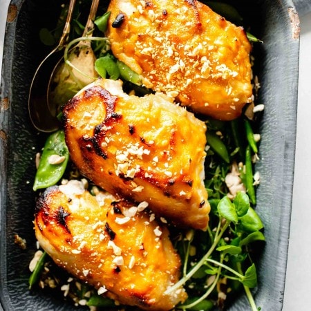 Overhead shot of three chicken breasts glazed with miso in grey pan served over pea pods.