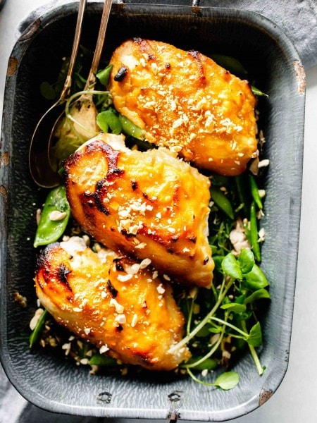 Overhead shot of three chicken breasts glazed with miso in grey pan served over pea pods.