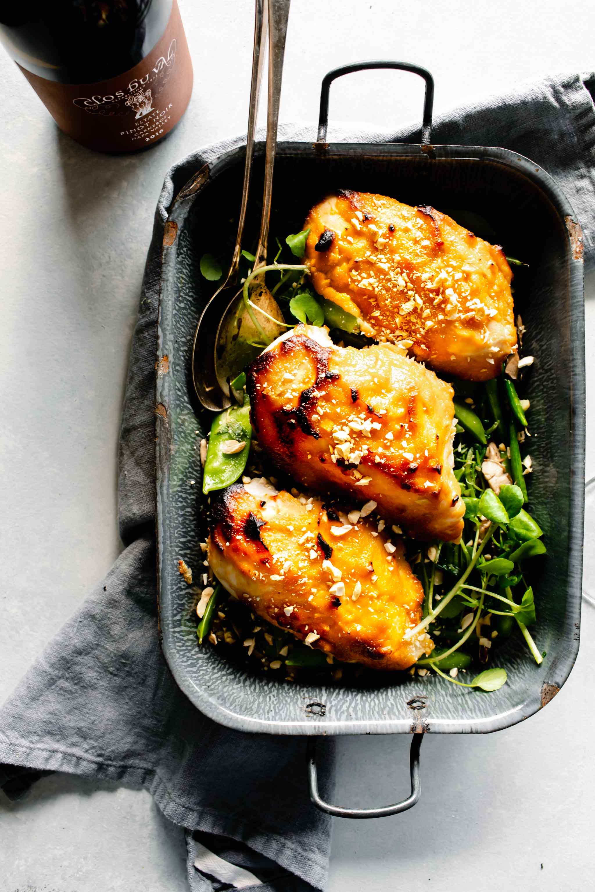 Overhead shot of three chicken breasts glazed with miso in grey pan served over pea pods.