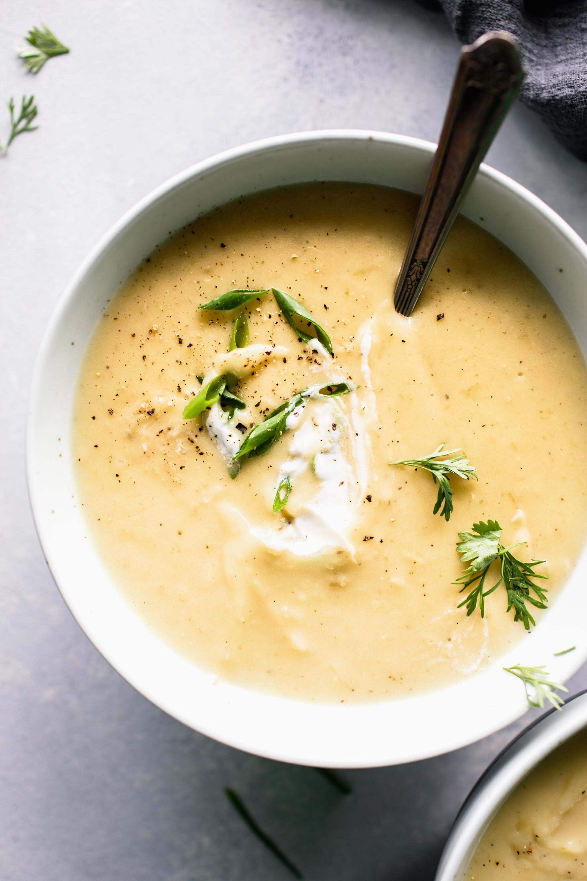 Two bowls of potato leek soup shot from overhead and garnished with green onions, parsley and a dollop of yogurt.