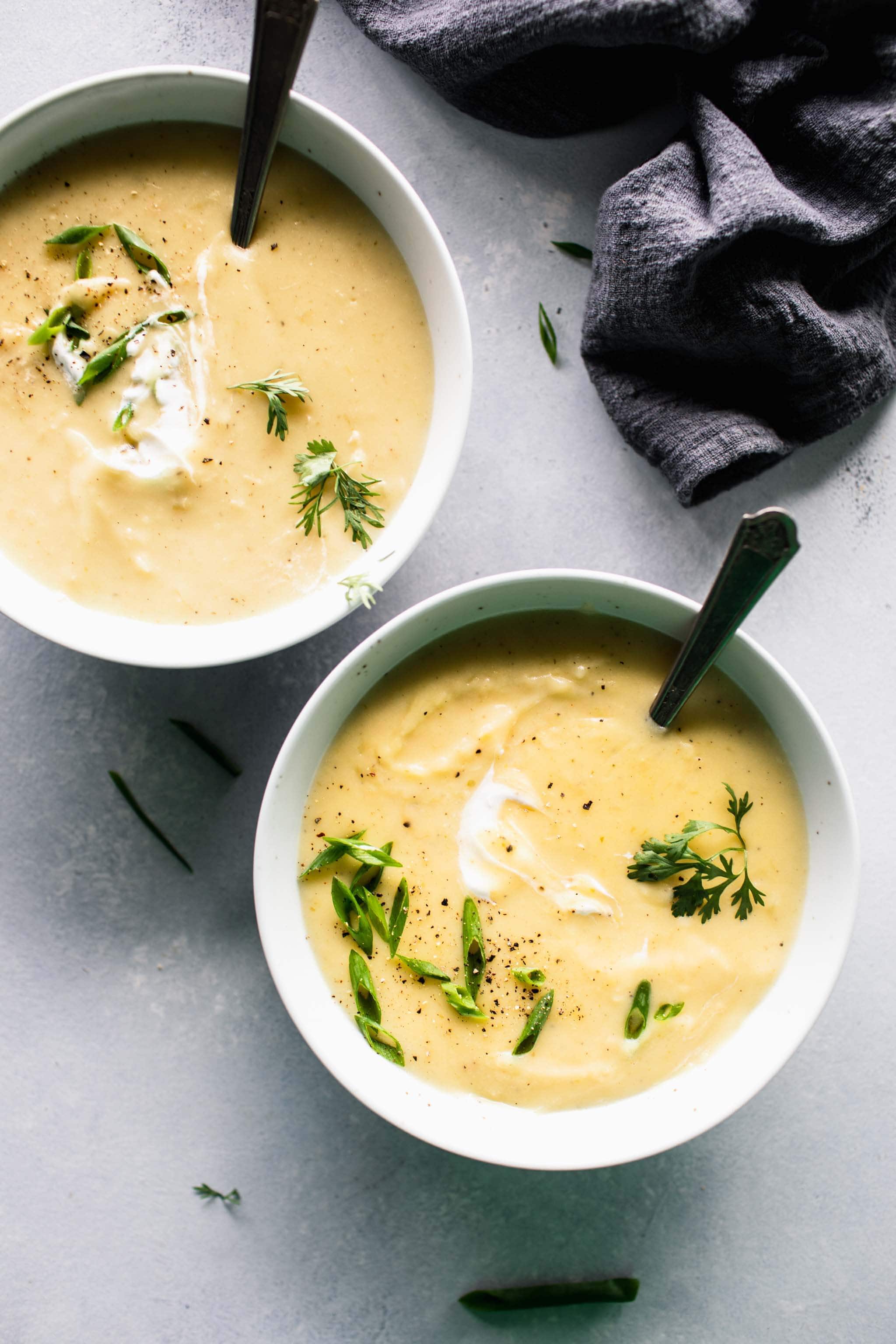 Overhead shot of two bowls of potato leek soup on table with grey dish cloth. 