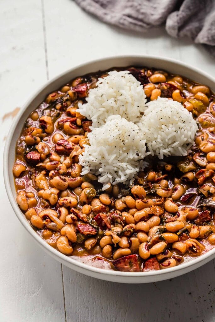 Side view of black eyed peas in bowl with scoops of rice on top. 