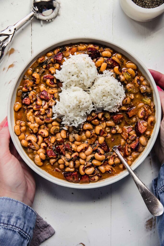 Hands holding bowl of cooked black eyed peas. 