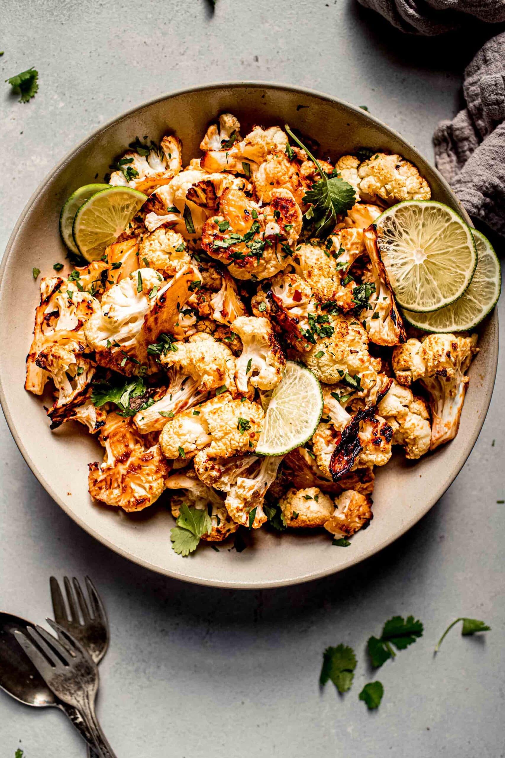 Prepared miso cauliflower in serving bowl with lime wedges and cilantro.