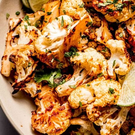 Overhead close up of miso cauliflower in serving bowl with lime wedges and cilantro.