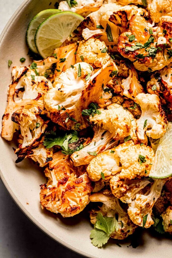 Overhead close up of miso cauliflower in serving bowl with lime wedges and cilantro.