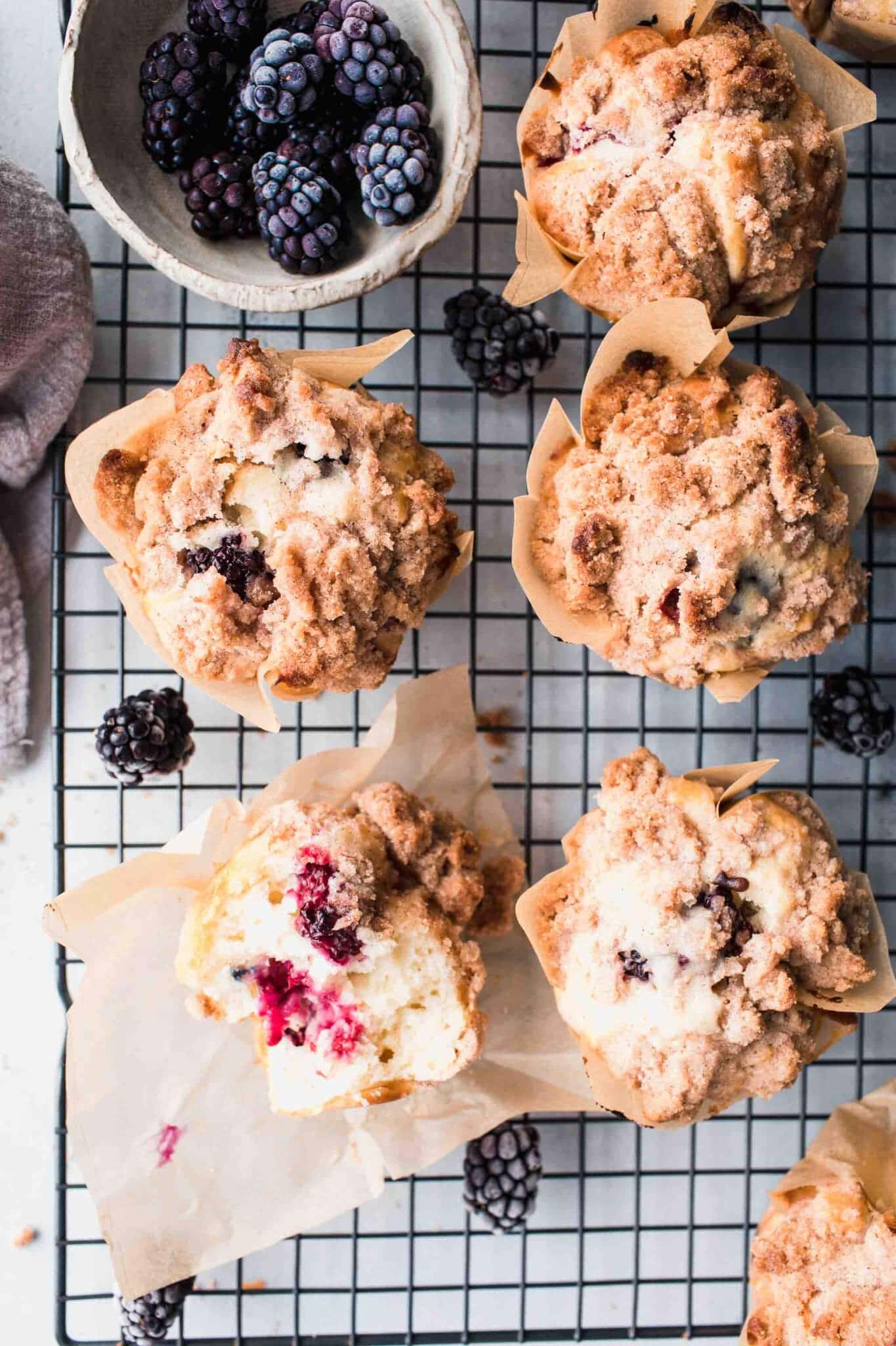 Overhead shot of blackberry muffins on cooling rack next to bowl of blackberries.