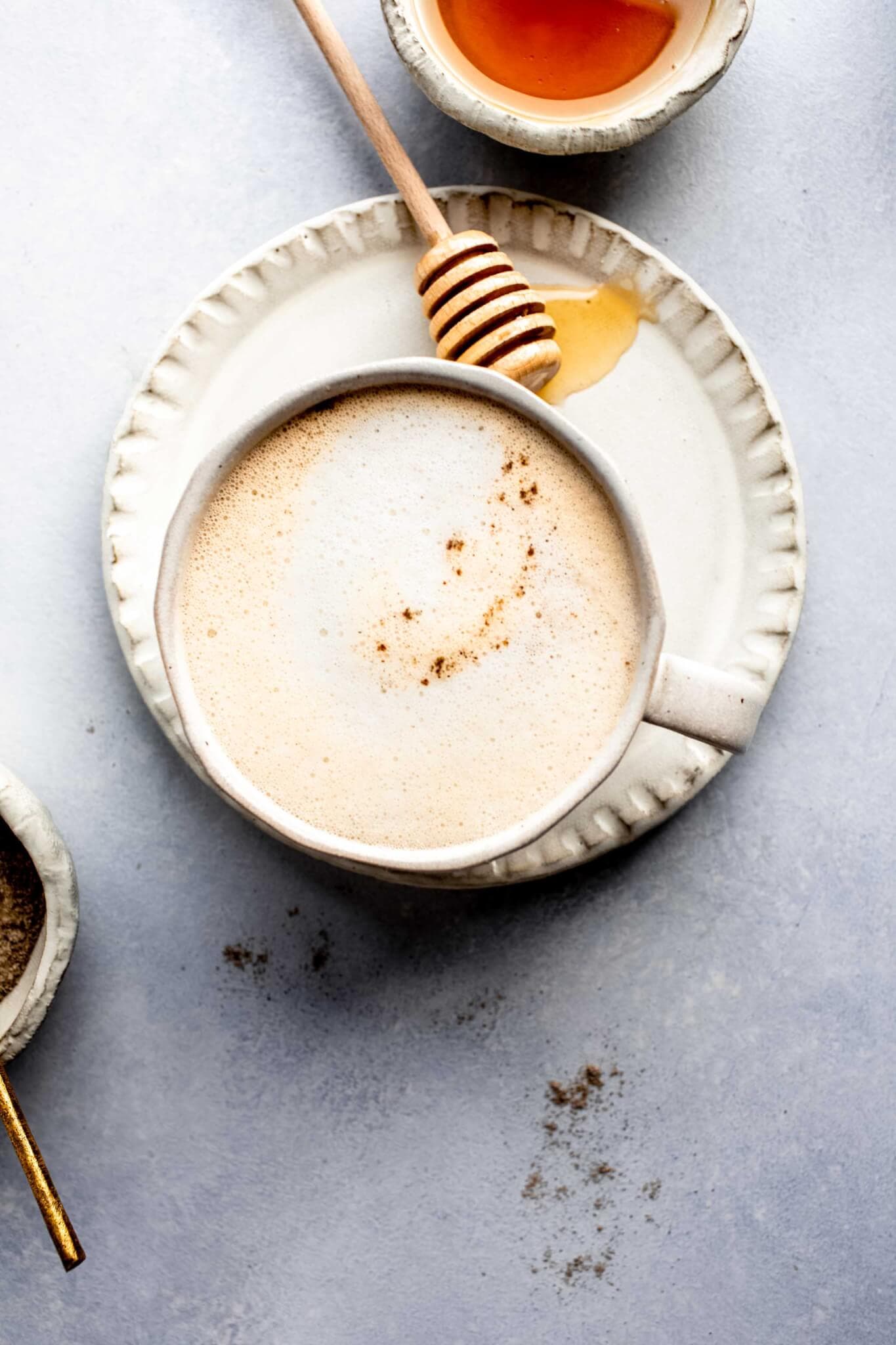 Overhead shot of cardamom latte next to honey wand and bowl of cardamom.