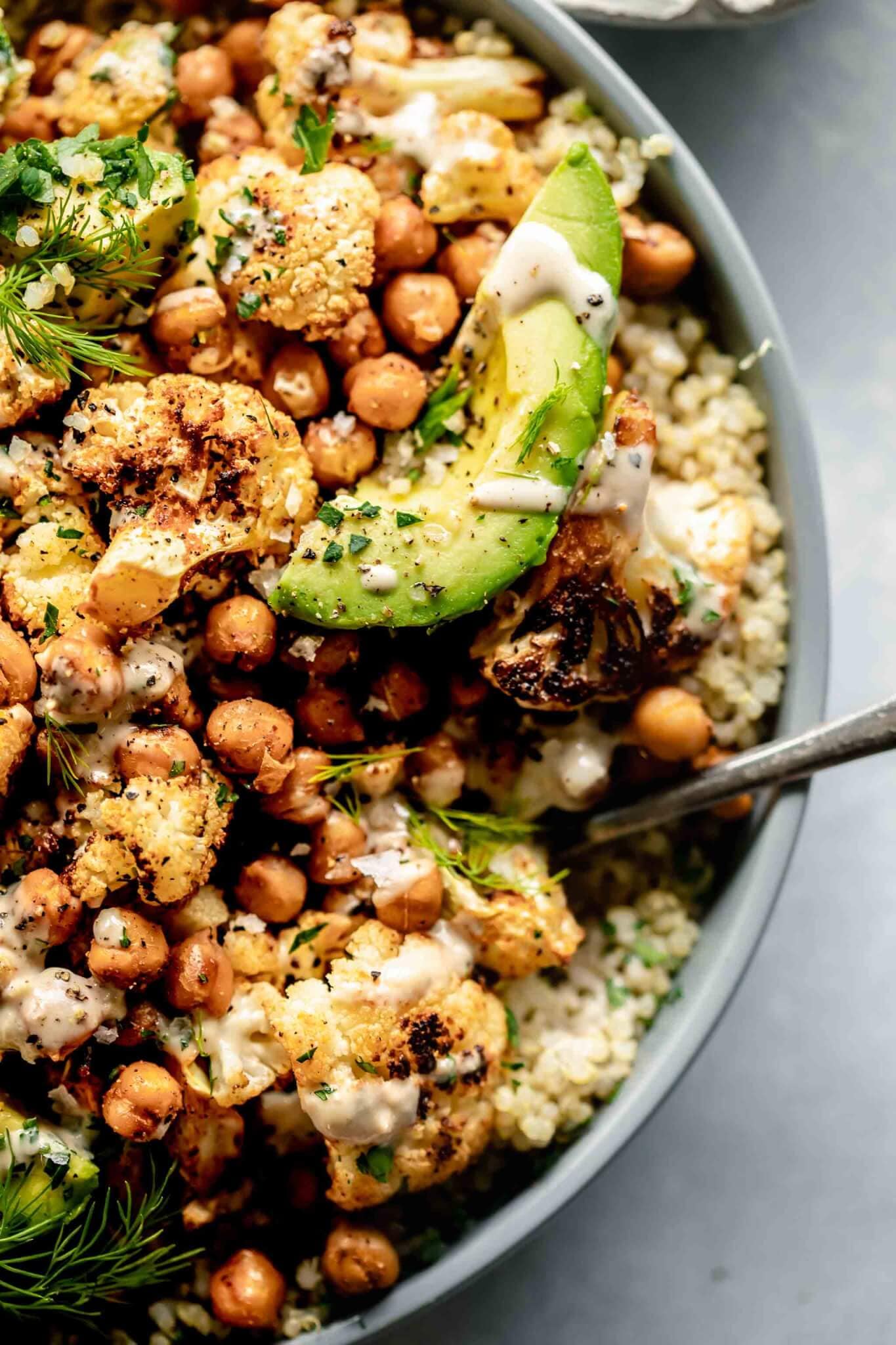 Overhead close up of bowl of quinoa salad in grey bowl with spoon topped with avocado.