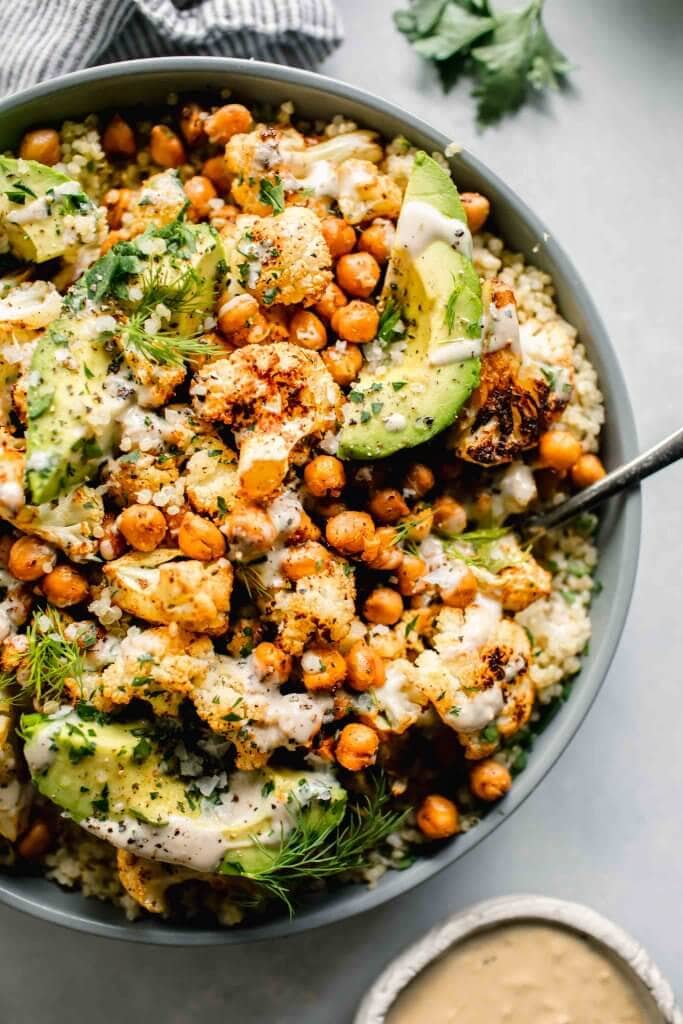 Overhead shot of roasted cauliflower salad in grey bowl with spoon next to small bowl of tahini dressing.