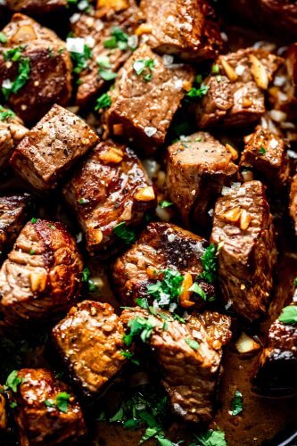 Overhead closeup of steak bites in skillet topped with garlic bits and parsley.