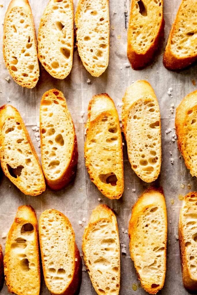 Baked crostini on baking sheet lined with parchment paper.