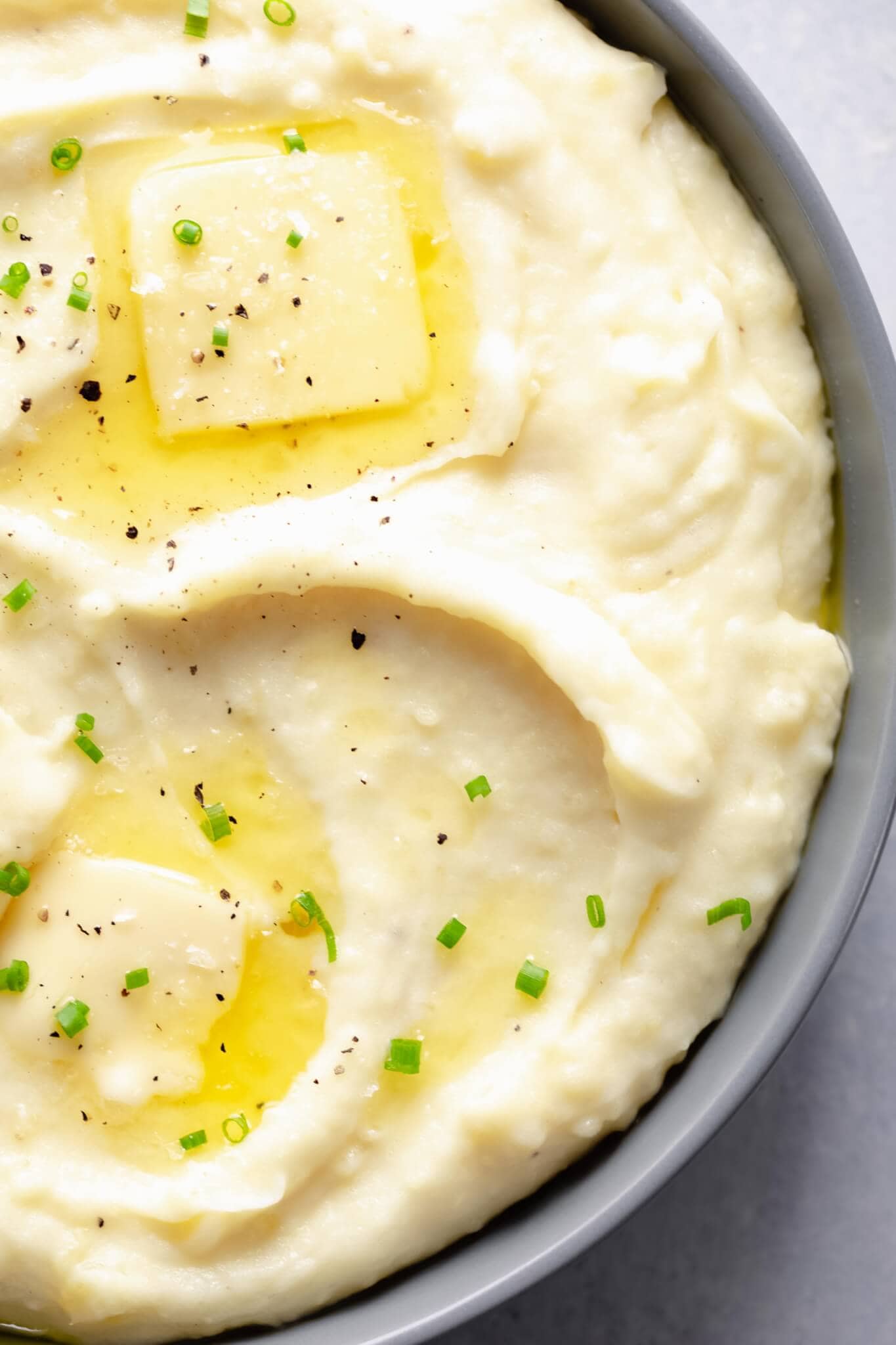 Overhead close up of instant pot mashed potatoes in grey bowl with two pats of melted butter & chives.