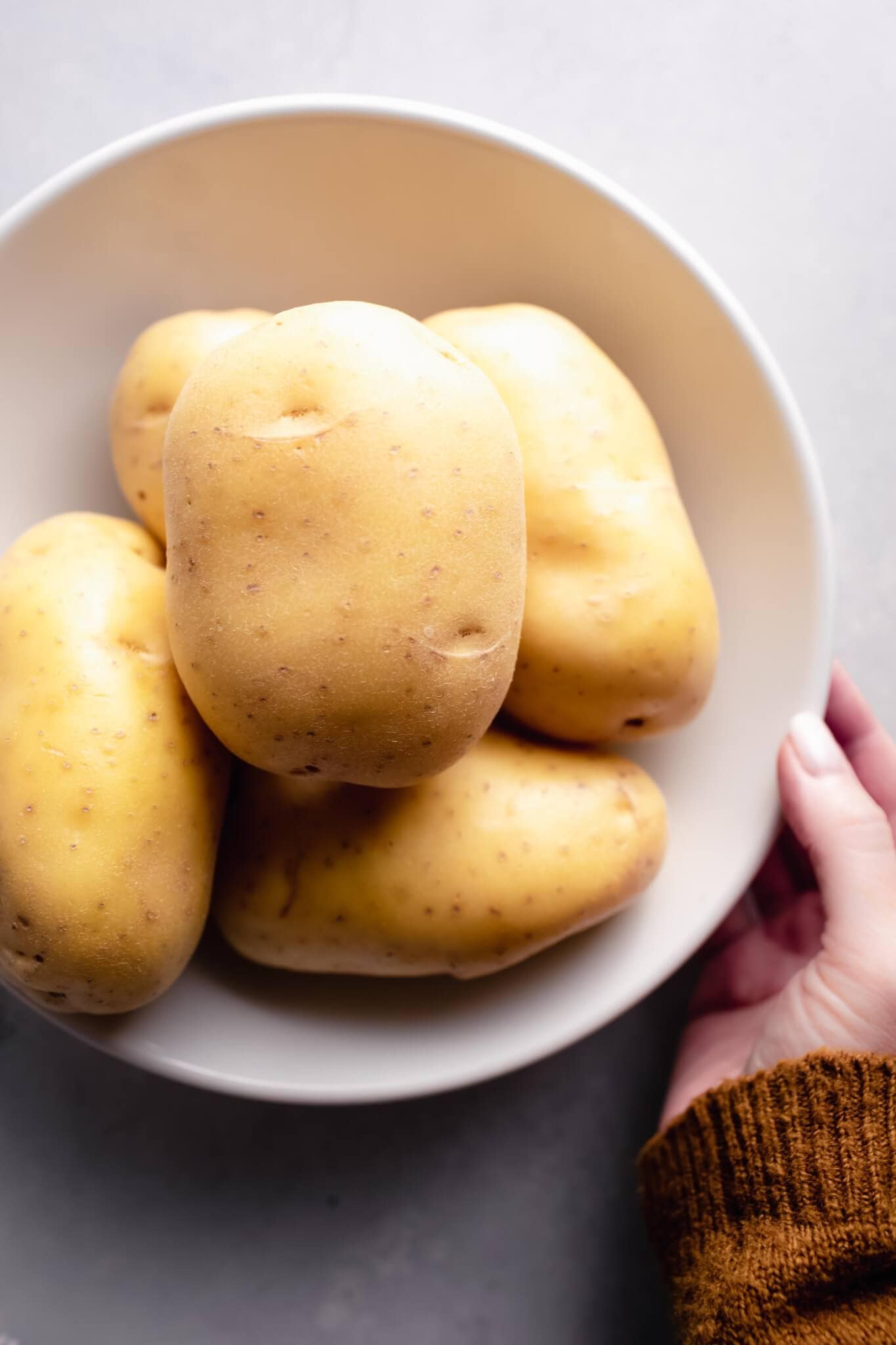 Hand holding bowl of potatoes before peeling.